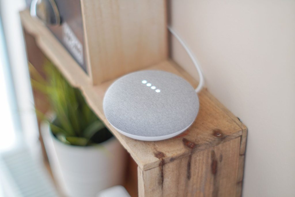 Розумна колонка Google Home Mini на дерев'яній поличці серед домашнього декору.