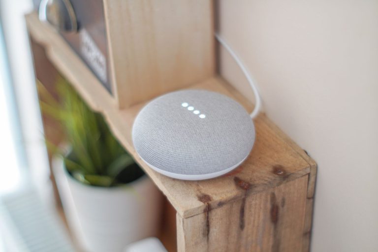 Розумна колонка Google Home Mini на дерев'яній поличці серед домашнього декору.